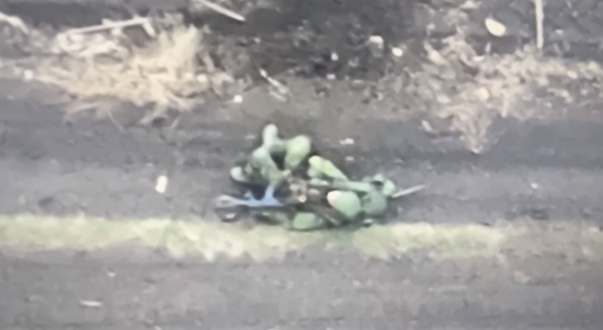 Russian is walking along dirt road. Plays dead when FPV approaches but is struck anyway, although it doesn't explode immediately. He rolls onto his back and shoots himself