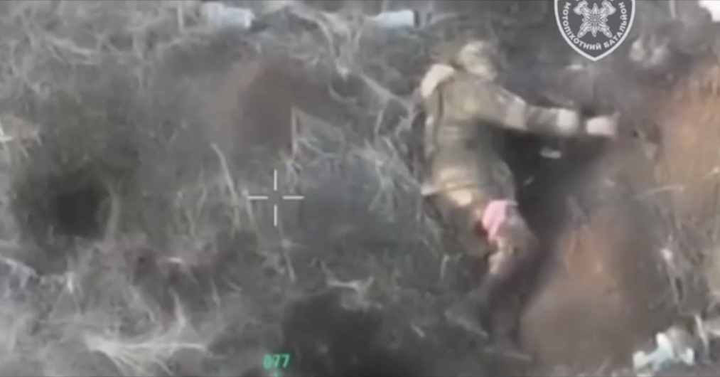 Russian lying on his side with red band on his leg and no helmet on shoots himself with AK