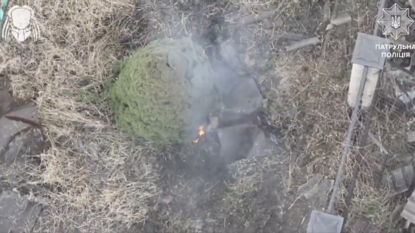 Russian is under drone drop attack, grabs some sheet as cover and crawls under pine tree, receives another hit. Few moments after something explodes under the sheet throwing both the sheet and his helmet off