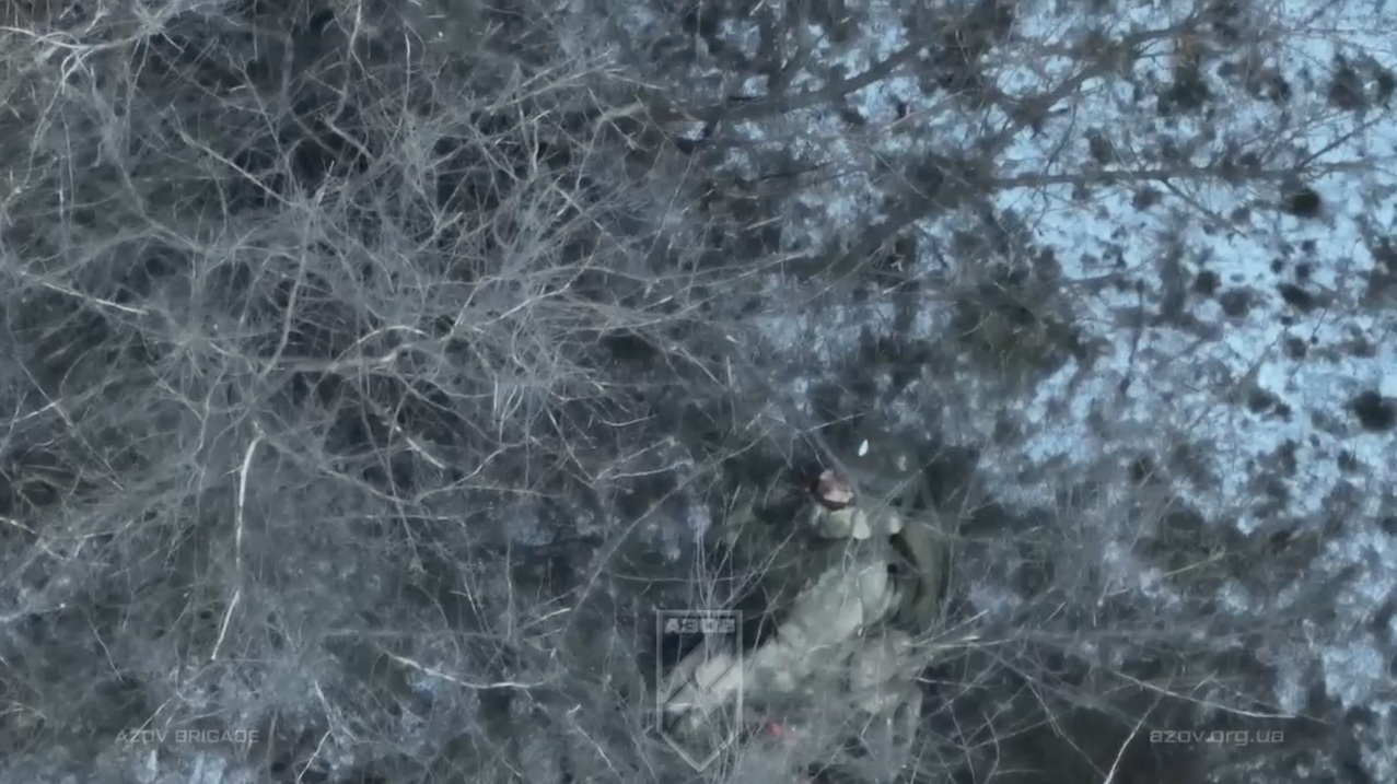 Russian is hiding under tree after unsuccessful attack on ATV, receives drone dropped grenade, it explodes near his head. Is seen shooting himself later on