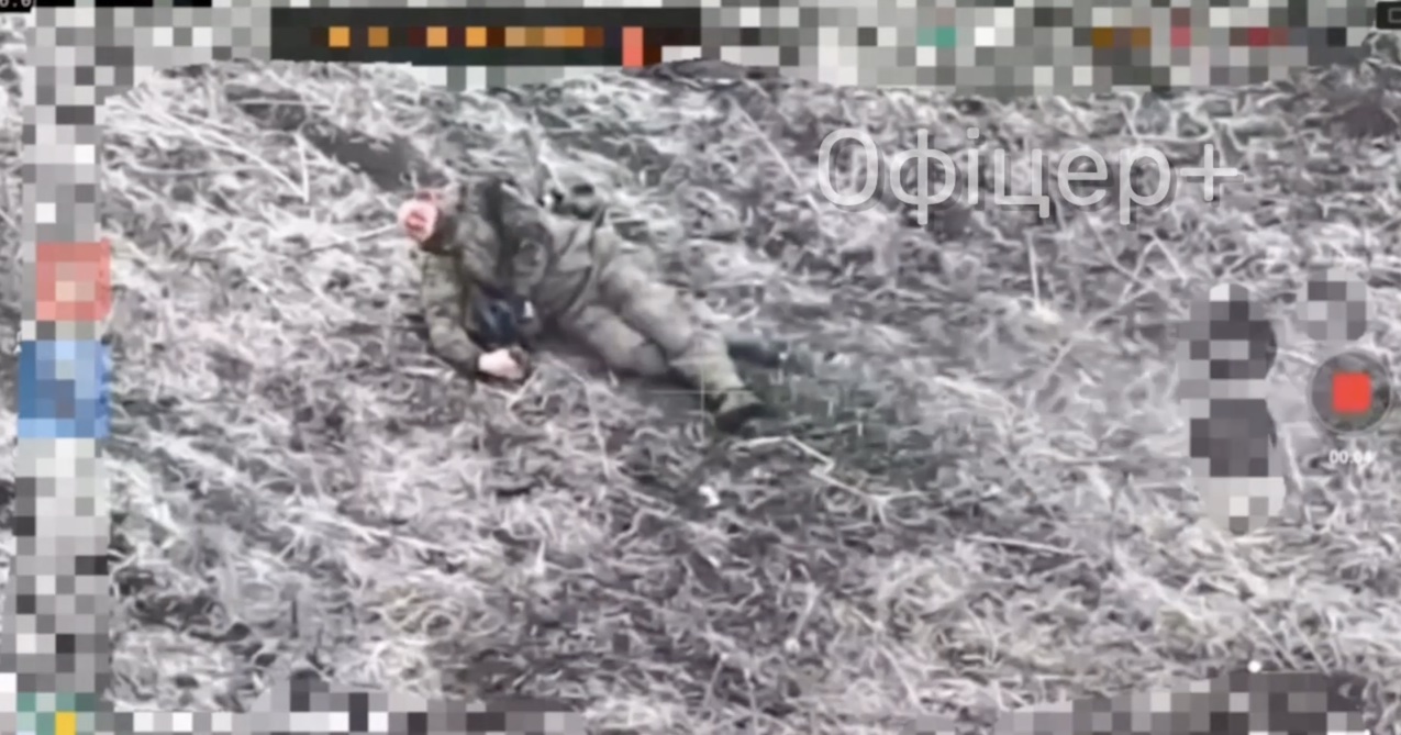 Russian lies on the ground visibly injured, apparently can't move half his body. Attempts to shoot himself with one hand but misses, tries again and misses again, turns to his back and tries one more time, still to no avail
