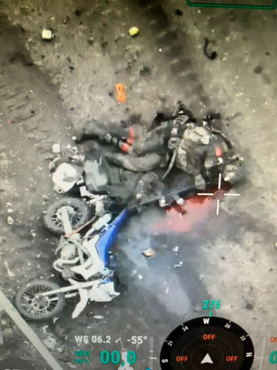 Photo of apparently dead Russian lying on the ground next to motorcycle. His leg injured, his AK pointed at his face with a lot of blood around, and his finger near the trigger
