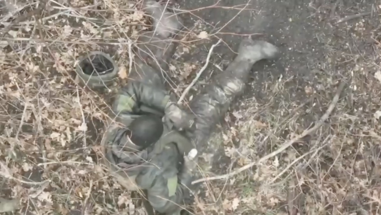 Russian sitting on the ground with his helmet off pulls the pin on his grenade, moves his belly armour out of the way and rolls over it