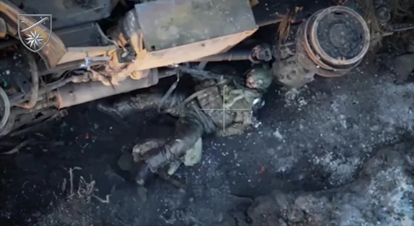 Russian hiding under flipped truck receives direct hit by a drone in his shoulder. He grabs his AK with his other hand and shoots himself