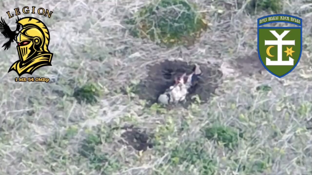 Equipped Russian soldier is seen from a distance lying on his back in fresh shell crater and shooting himself