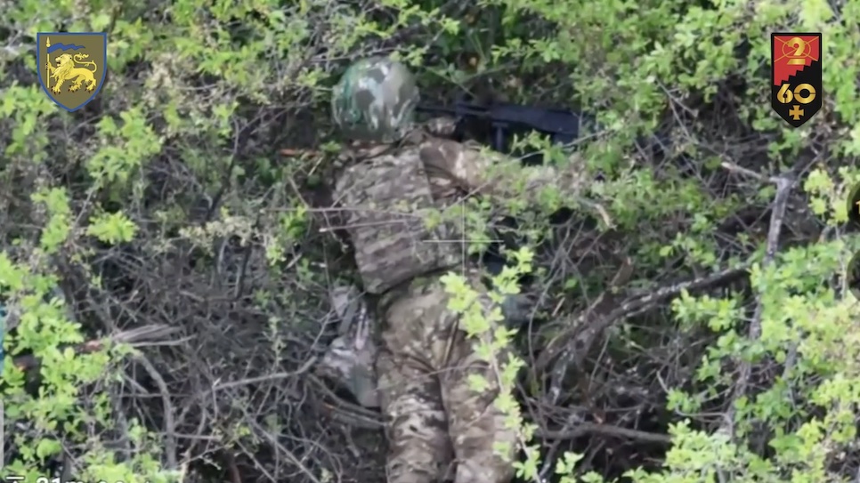 Fully equipped Russian soldier lies on his belly in the bushes with modern AK variant, tries to shoot himself in the temple but it won't fire. He reloads it and shoots again