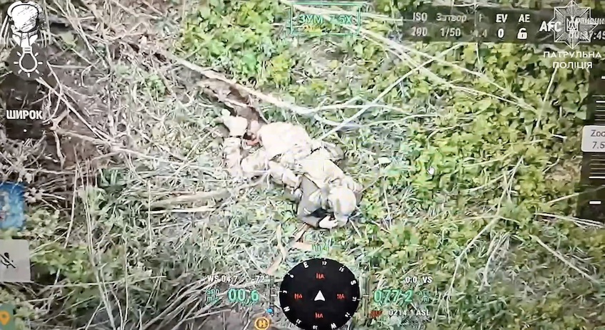 Russian receives close hit by a drone dropped grenade while walking among trees, later is seen lying on the ground, one of his legs is covered with blood. He pulls the pin on his own grenade and detonates it besides