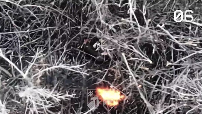 Russian soldier is seen through tree branches lying on his side and shooting himself while something is on fire nearby. Footage is likely months old