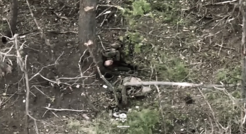Russian soldier walks past wounded comrade leaning against a tree. Few moments later the comrade puts his rifle under his chin and fires multiple shots into his head
