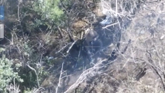 Russian is seen from above sitting in what looks like a treeline. He reloads his AK rather routinely, fires test round into the ground, then shoots himself and falls back. As he pulls the trigger, bullet makes a visible exit hole in his helmet.