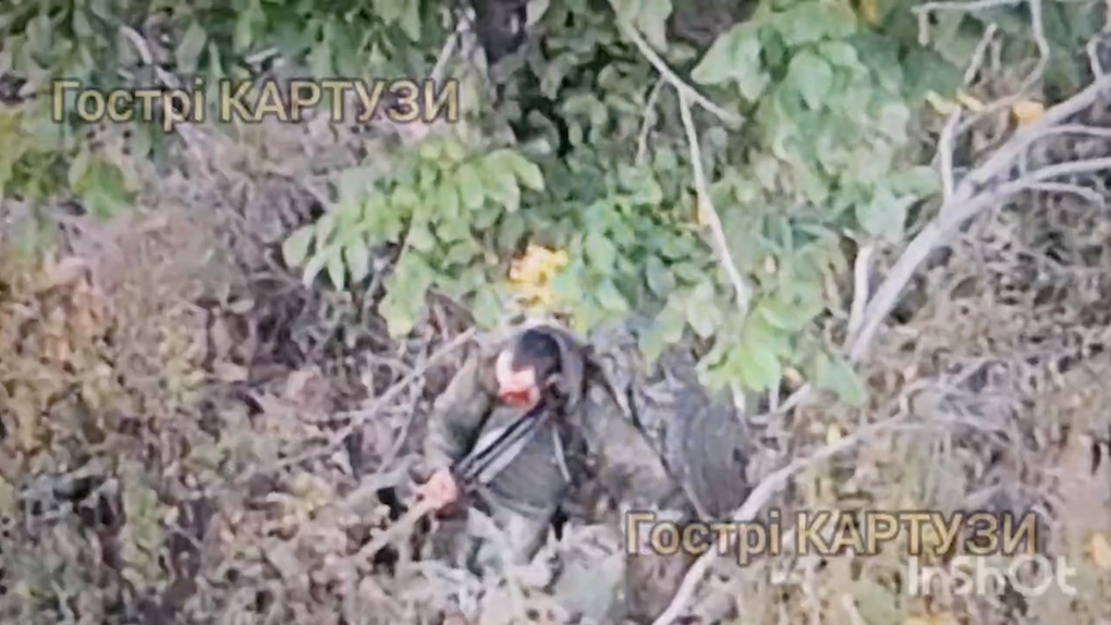Russian walks down the road among ruins, suddenly drops his backpack and hides under tree. He takes off his helmet, moves around chaotically, receives close hit in the meantime. He then grabs AK and shoots himself but is very much alive, appears to try again but with no visible effect. Eventually is seen with half of his face in blood and making himself comfortable on the ground