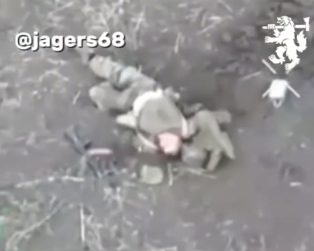 Russian lies on the ground next to his dead comrade, presumably after FPV attack. He moves his hands in the air frantically, grabs AK and shoots himself towards his face barely hurting himself. Tries once again, this time he doesn't seem to be moving any more