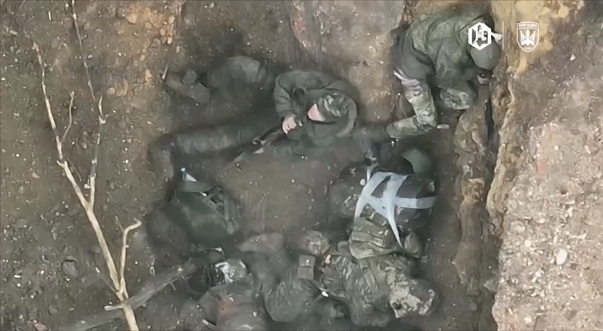 Trio of Russians are hiding in improvised pit inside anti-tank ditch, receive drone drop. One of them grabs his AK and shoots himself with no hesitation to gruesome aftermath. The other two get FPVed soon after.