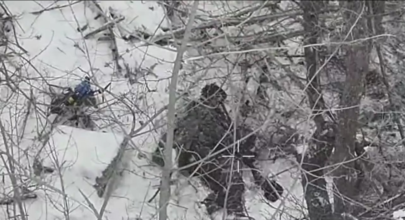 Russian with no helmet lies under the tree next to unexploded FPV on the snow, he points AK at his forehead, video freezes for several seconds until he's seen apparently dead