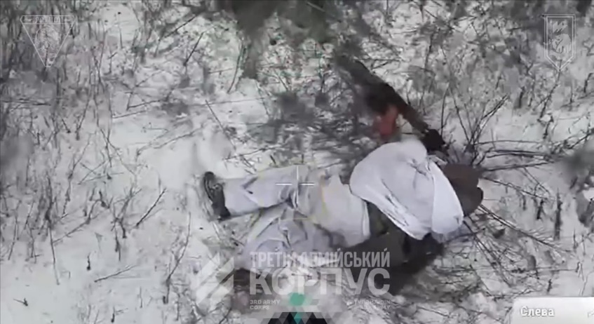 Russian is seen lying on the snow in winter camouflage and shooting himself with AK, his helmet flies off as he pulls the trigger