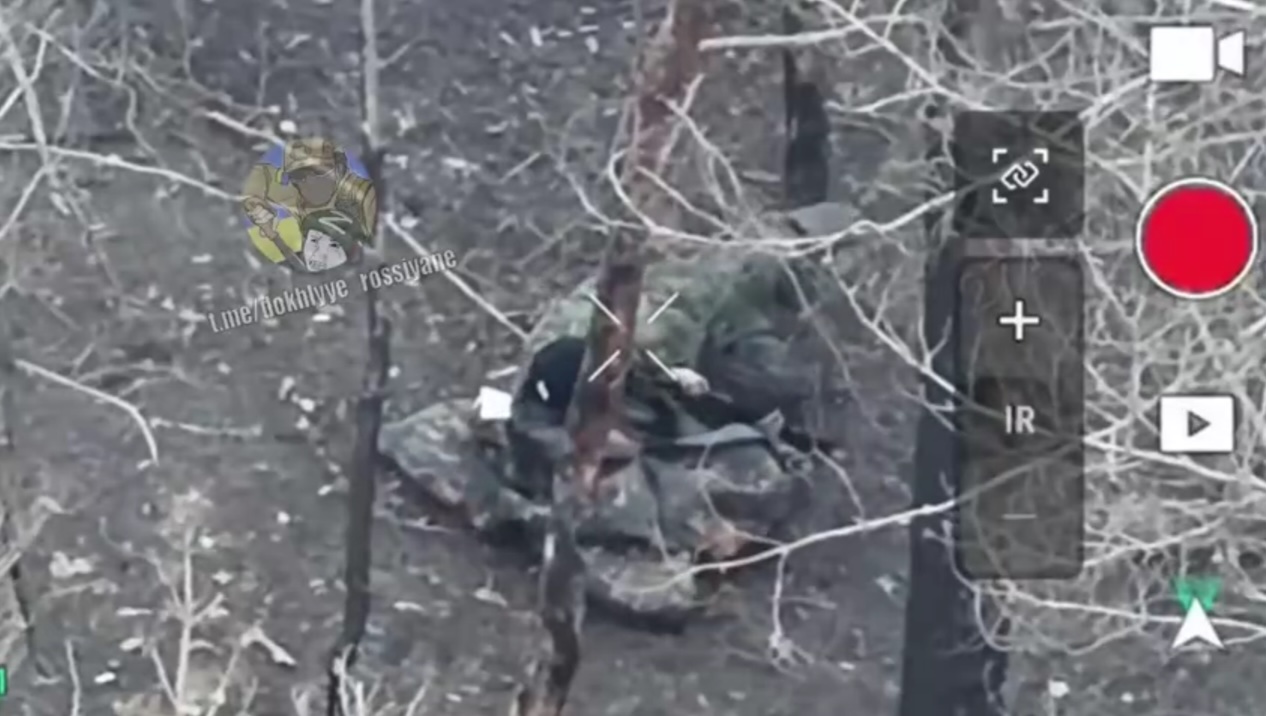 Russian soldier shoots himself while lying on some kind of garment among trees. The shot tears the hat off his head revealing wound