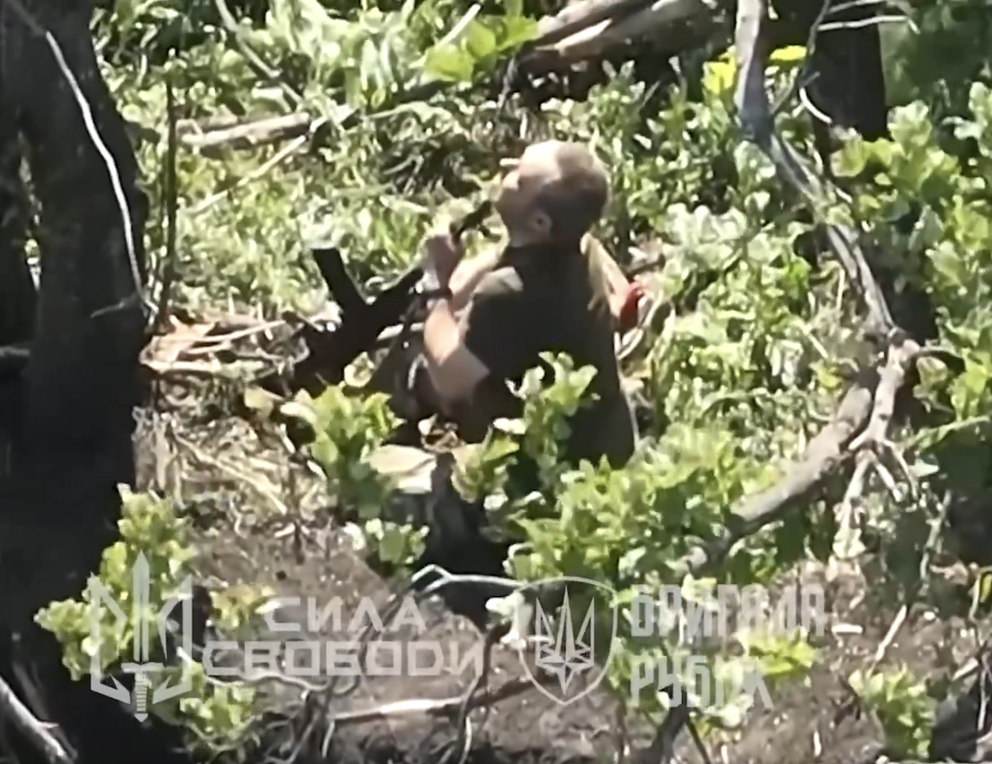 Russian soldier sitting in foliage with no helmet shoots himself in the head